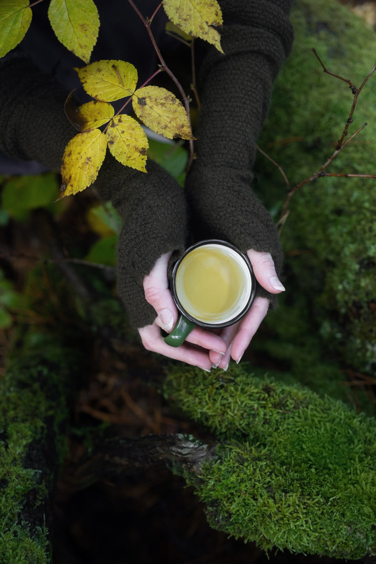 Drinking AGASAGA herbal tea in the cozy forest, holding a teacup in hands with gloves.