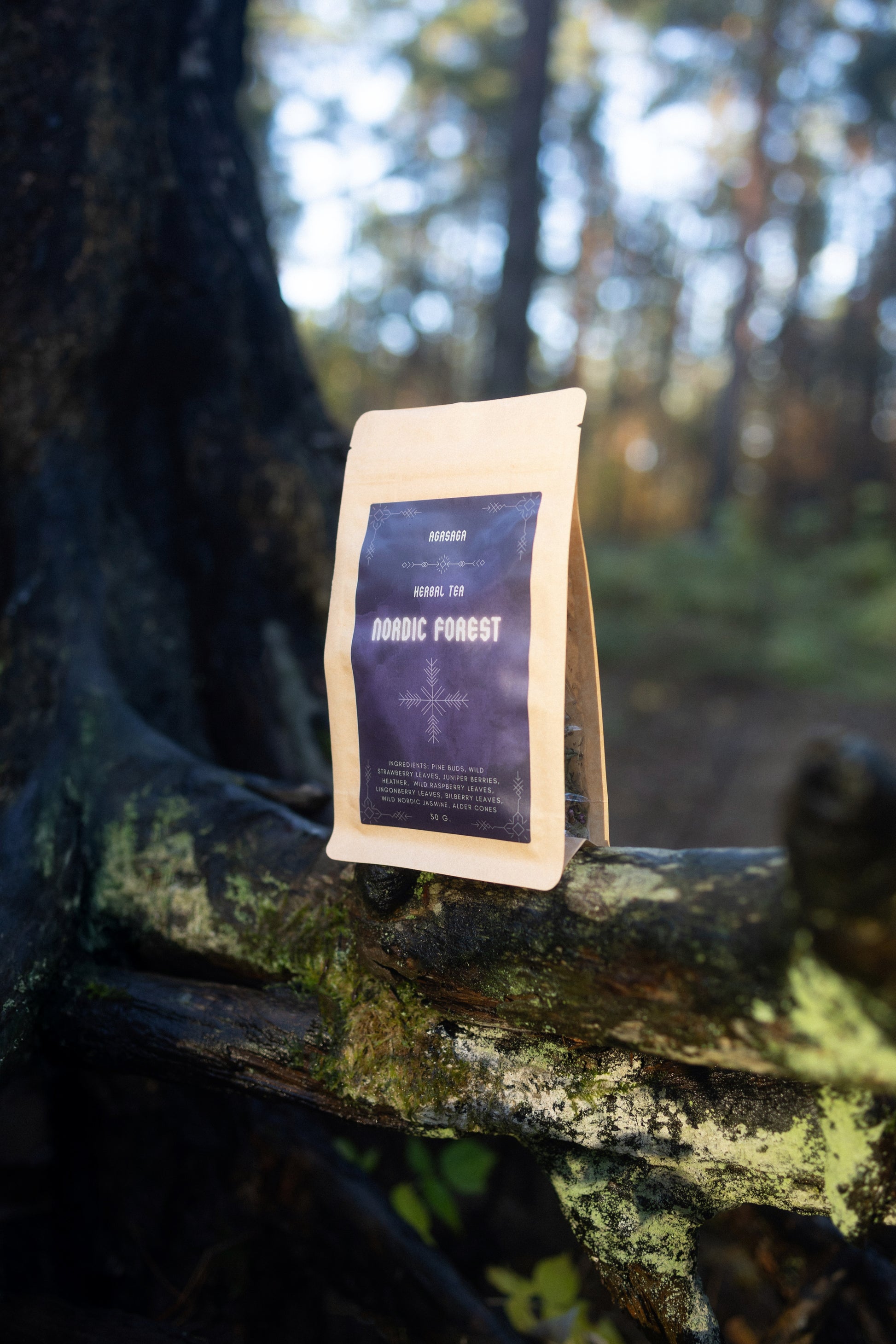 Packaging of AGASAGA Wildcrafted Nordic herbal tea with juniper, heather, and forest leaves arranged on a tree branch.